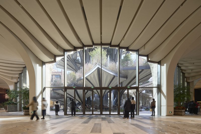 Entrance lobby with ribbed cream ceiling and full-height glazed doors overlooking the atrium with visitors passing through