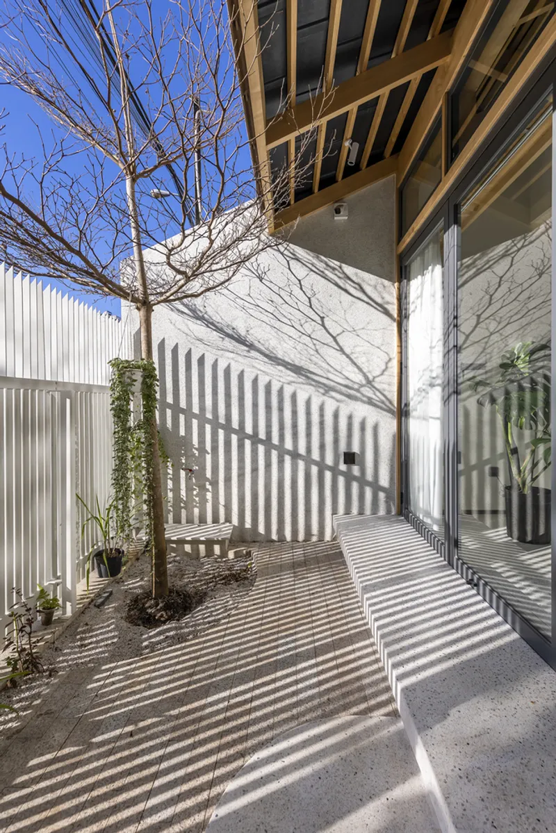 Exterior courtyard with vertical corrugated metal screens, bare winter tree, and planted beds in bright sunlight