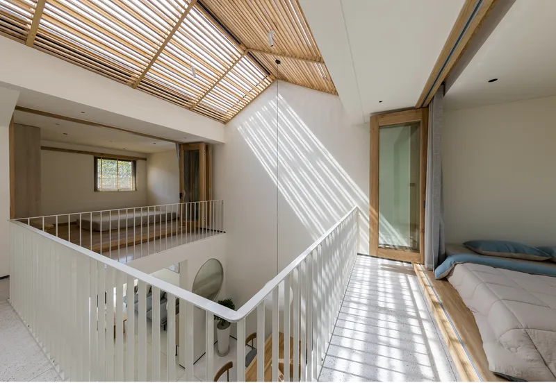 Upper floor bedroom alcove with timber flooring and dramatic light stripes from the slatted roof above