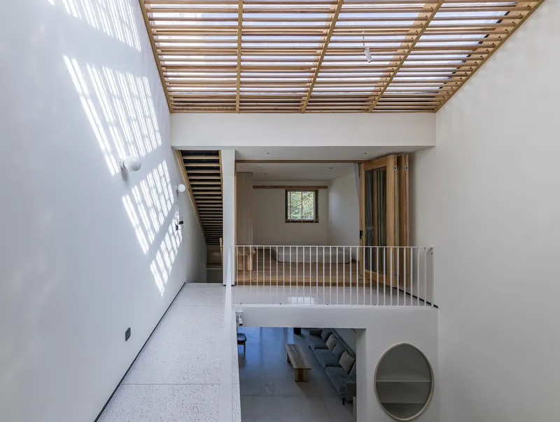 Double-height interior with timber slatted skylight casting linear shadows across white walls and terrazzo floor