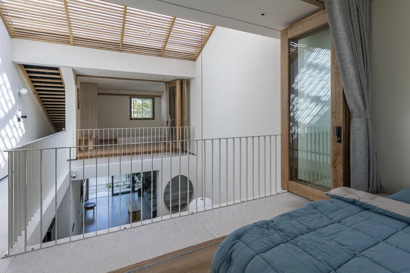 Upper level bedroom overlooking the double-height space with vertical metal railings and timber-framed doors