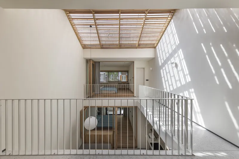 Interior staircase landing with metal railings beneath a timber slatted skylight and bright diagonal shadows