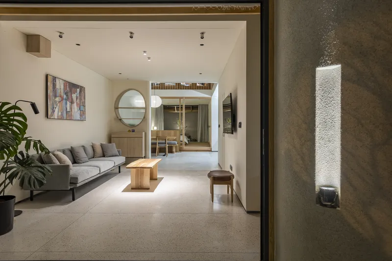 Ground floor living room looking through arched opening toward dining area with circular mirror and potted plant