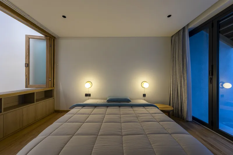 Bedroom with low platform bed, paired wall sconces, and sliding glass doors opening to a terrace at dusk