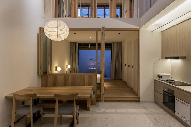 Open-plan dining area and kitchen at dusk with paper globe pendant and view to mezzanine above