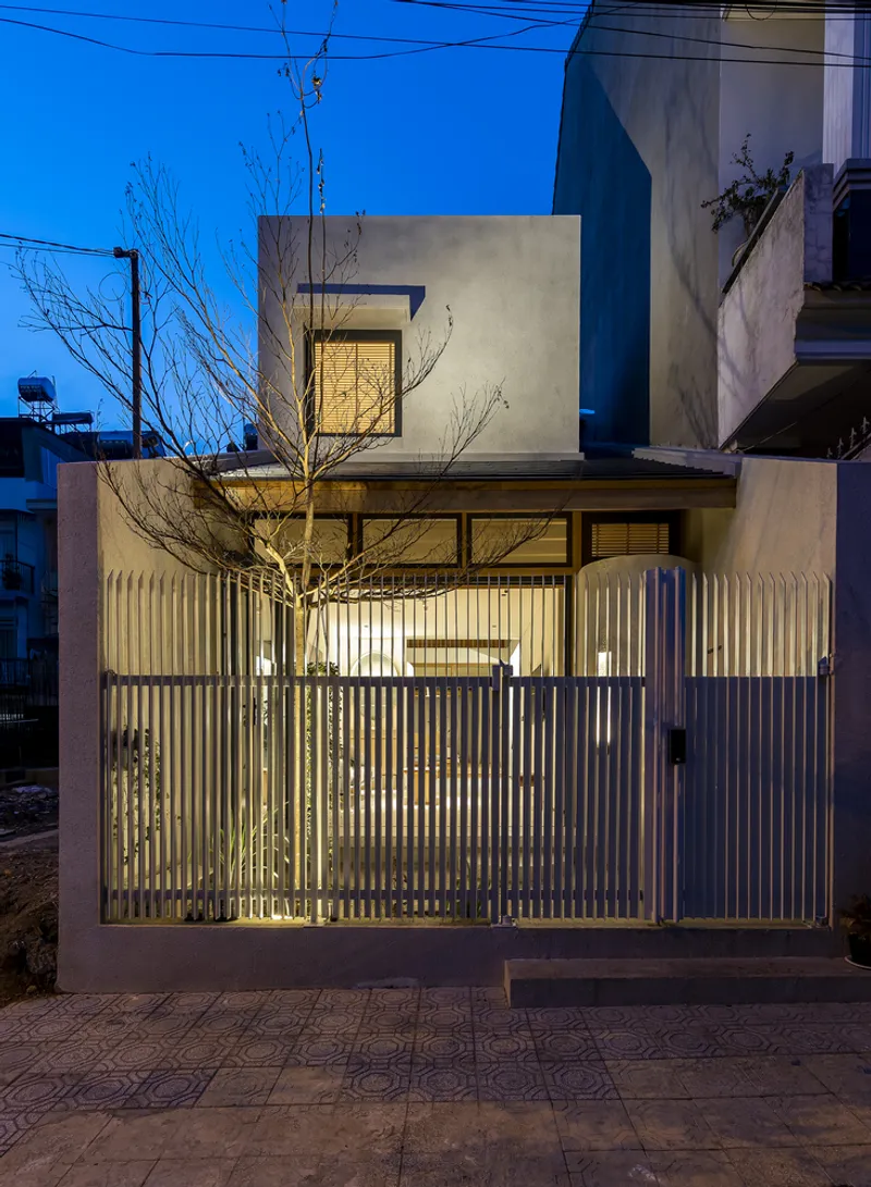 Street facade with vertical slatted metal gate and illuminated interior beyond a bare tree at dusk