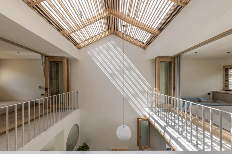 Double-height void with slatted timber skylight casting striped shadows across white walls and metal railings