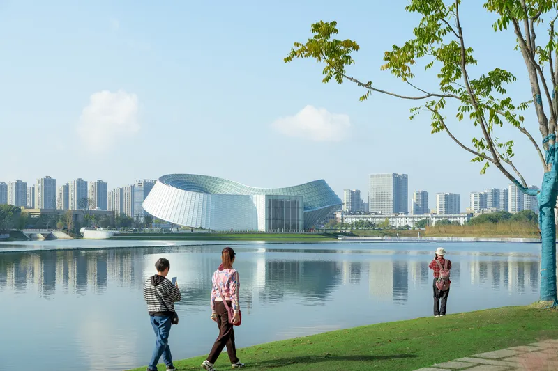View across the lake of the white and blue ribbed facade with pedestrians on the shoreline