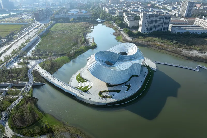 Aerial view of the curved building volumes on an island surrounded by water and urban fabric