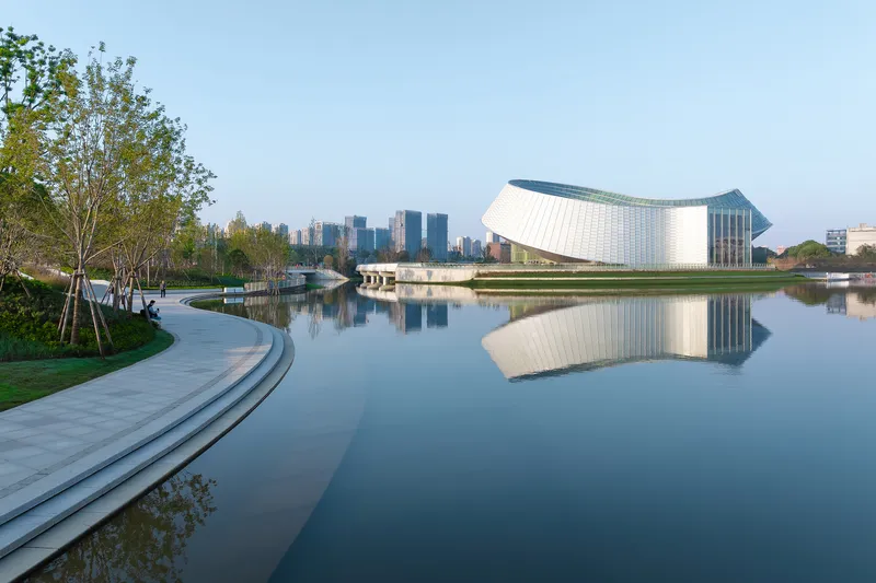 Lakeside promenade with stepped concrete seating and the white building reflected in still water at dusk