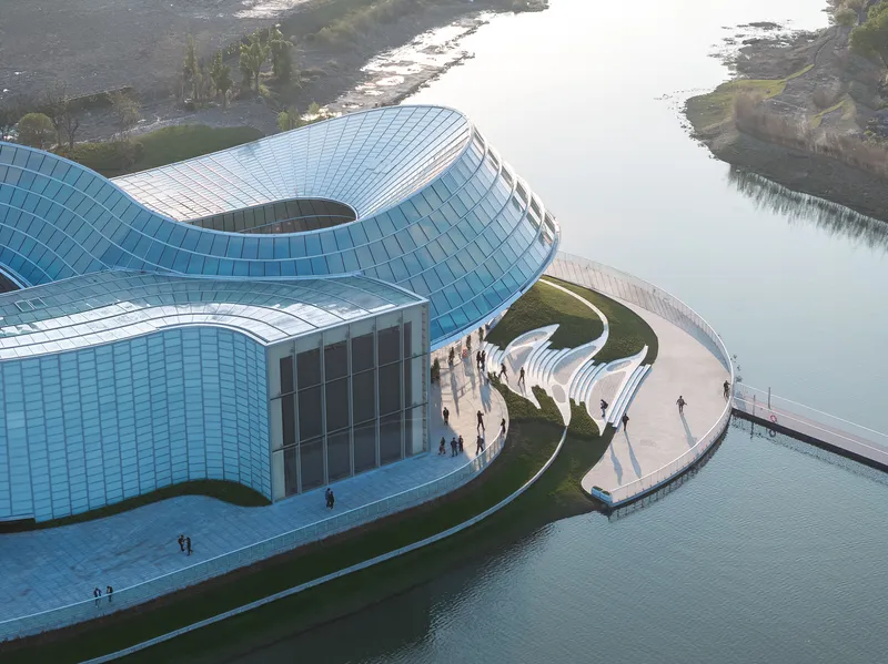 Aerial view of the blue tiled facade volumes and entry plaza with visitors gathering below