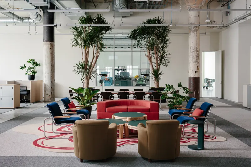 Circular seating cluster with colorful lounge chairs around patterned carpet beneath tall potted dracaena plants