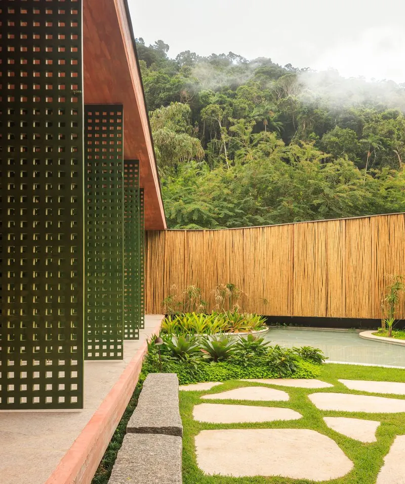 Courtyard with perforated screen walls and stone stepping pads in lawn beside reflecting pool under misty hills