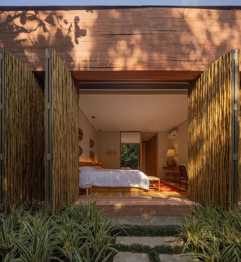 Bedroom opening to courtyard with vertical bamboo doors and stone path through planted ground cover