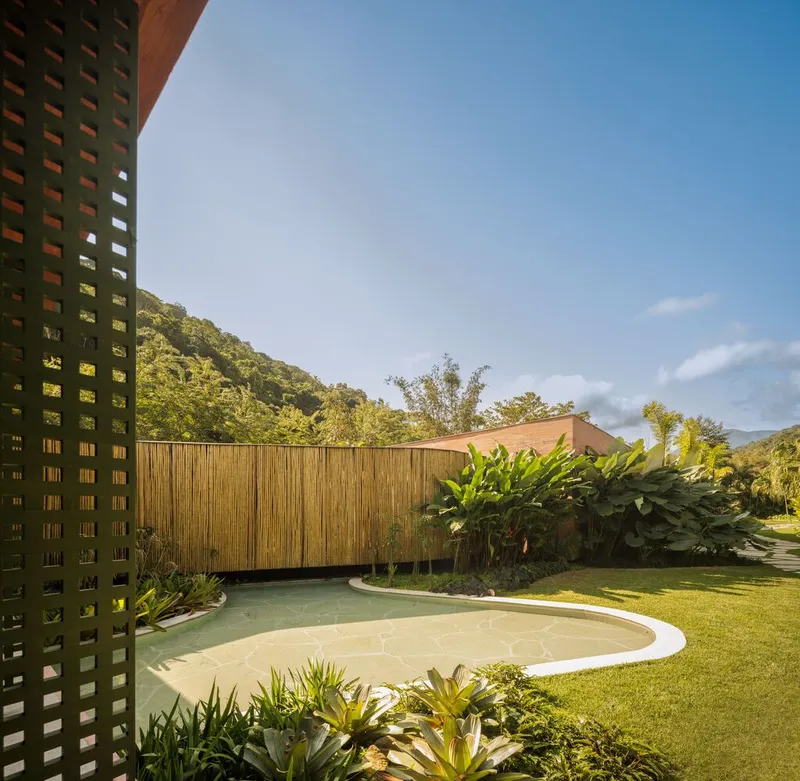 Curved pool with lawn and perforated brick screen wall beneath hillside vegetation