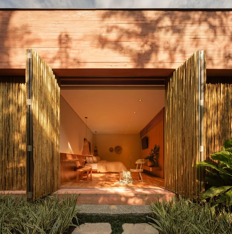 Entry threshold framed by vertical bamboo doors with dappled tree shadows on horizontal timber cladding