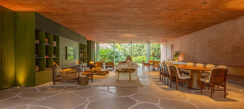 Open-plan living and dining space with timber ceiling, stone floor, and glass wall opening to garden