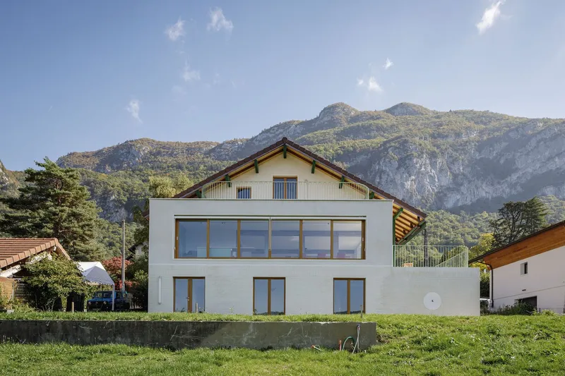 Garden facade: white rendered villa with new ground-floor extension, timber-framed windows, mountains behind
