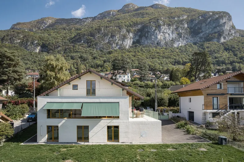 Elevated view: the villa with green retractable awning, white brick extension below, Annecy mountains beyond