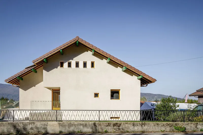 Street side: original villa form with pitched roof, small windows, white render, metal railing