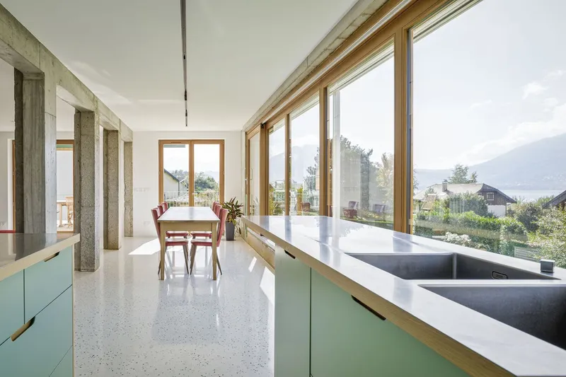 Kitchen counter: sage green cabinets, terrazzo countertop, full-width window looking to garden and lake hills
