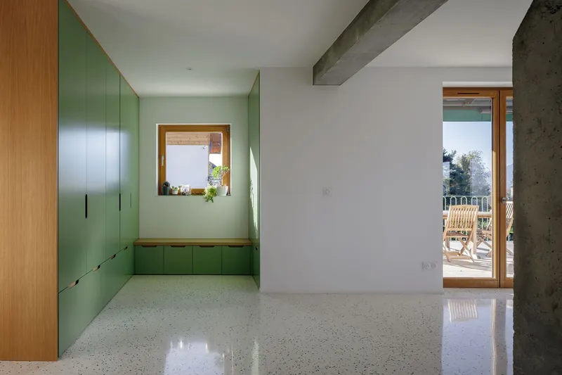 Children's room: sage green built-in cabinetry with timber bench, square interior window, terrazzo floor