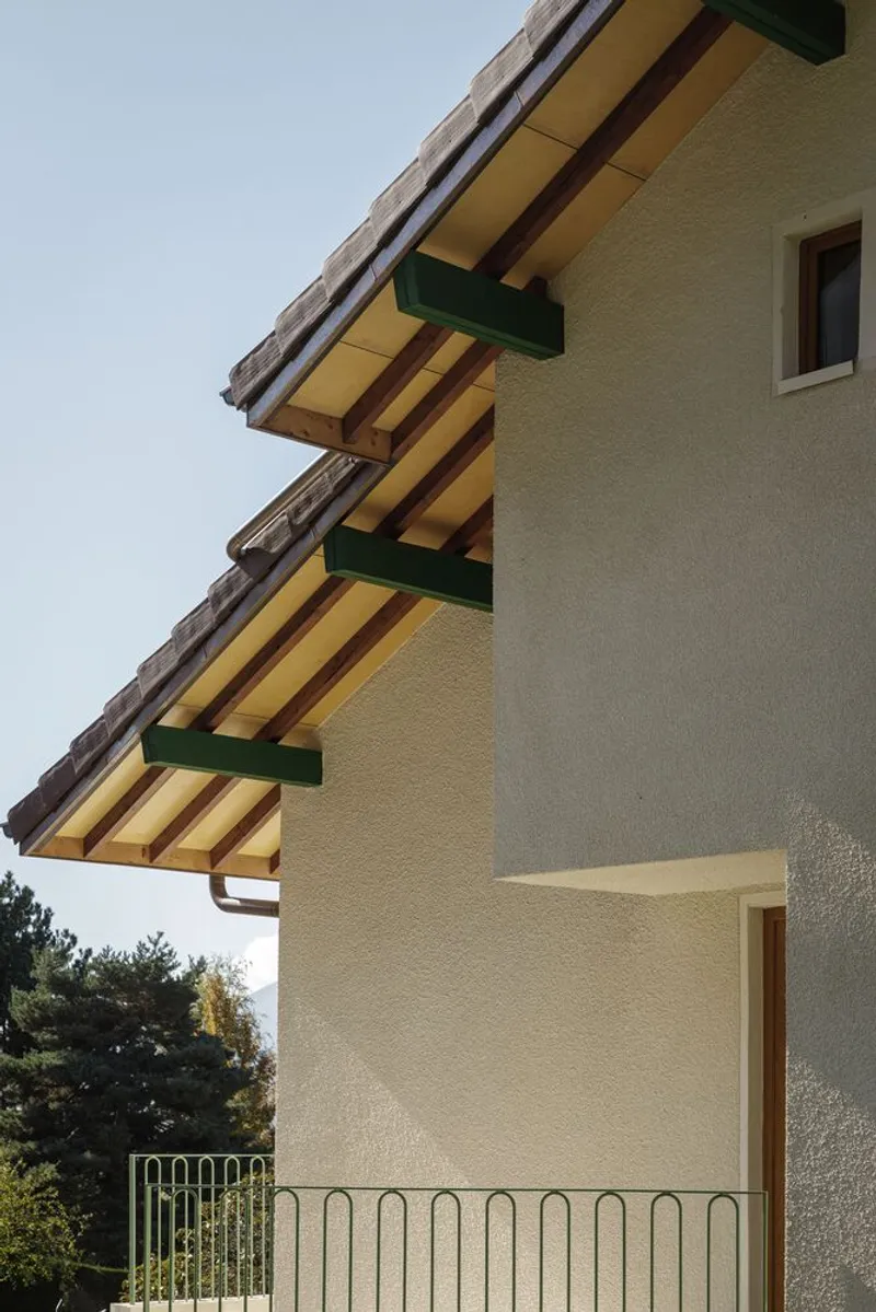 Eaves detail: exposed timber rafters painted yellow, green gutter brackets, rendered gable
