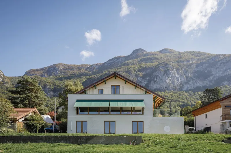 Full garden view: the complete villa with mountains behind, green awning, white brick base, lawn