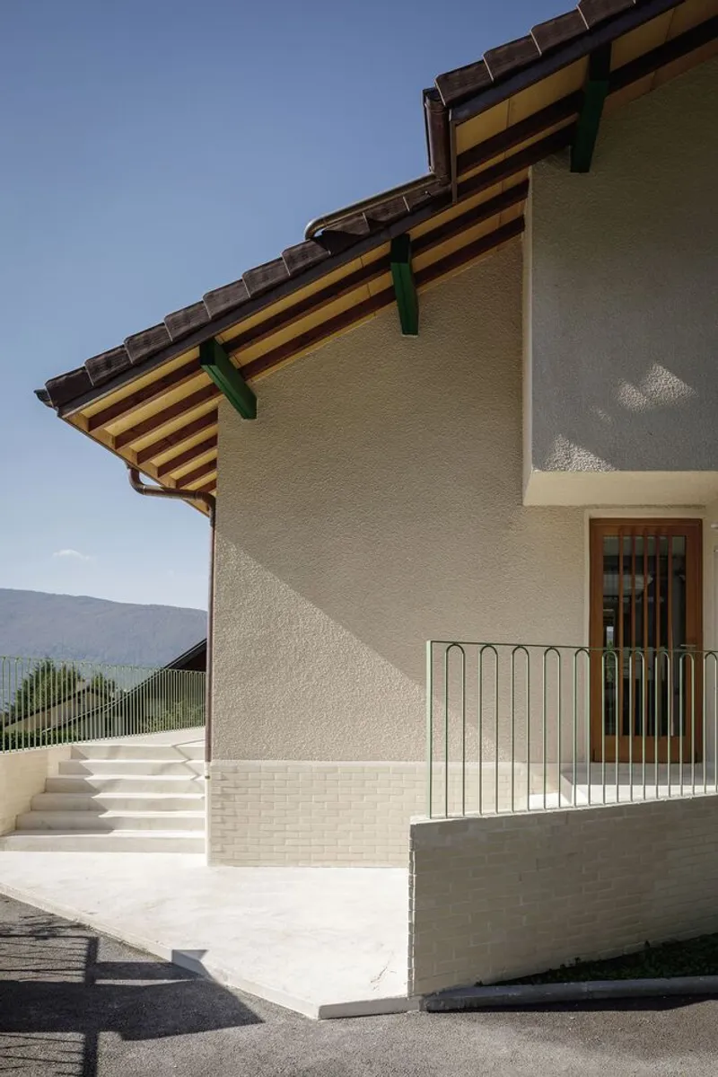 Entry side: concrete stair, timber door, exposed rafters, balcony railing shadow