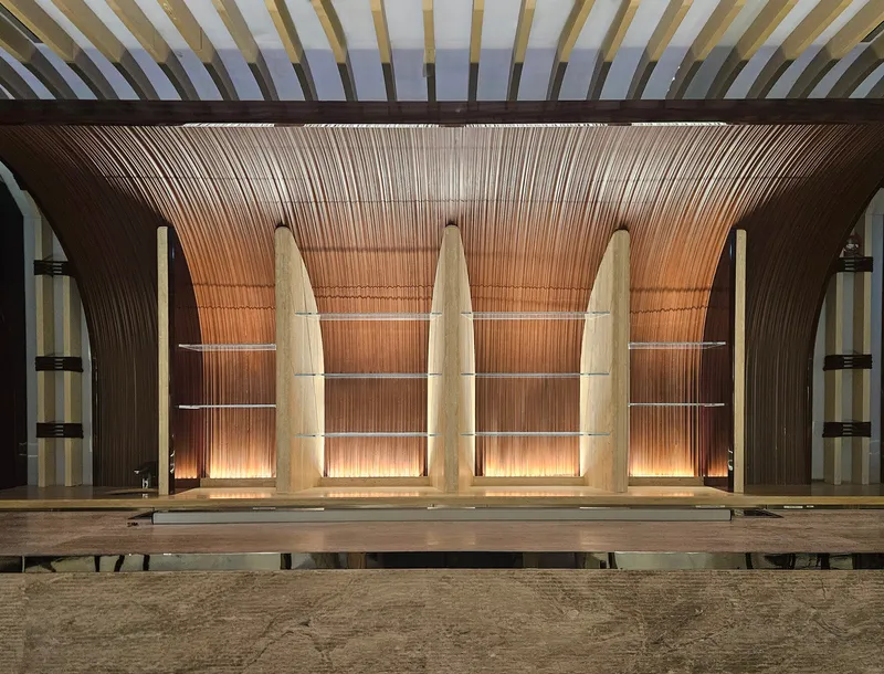 Nalu ground floor at night: wave-form timber columns lit from below, slatted ceiling, warm tones