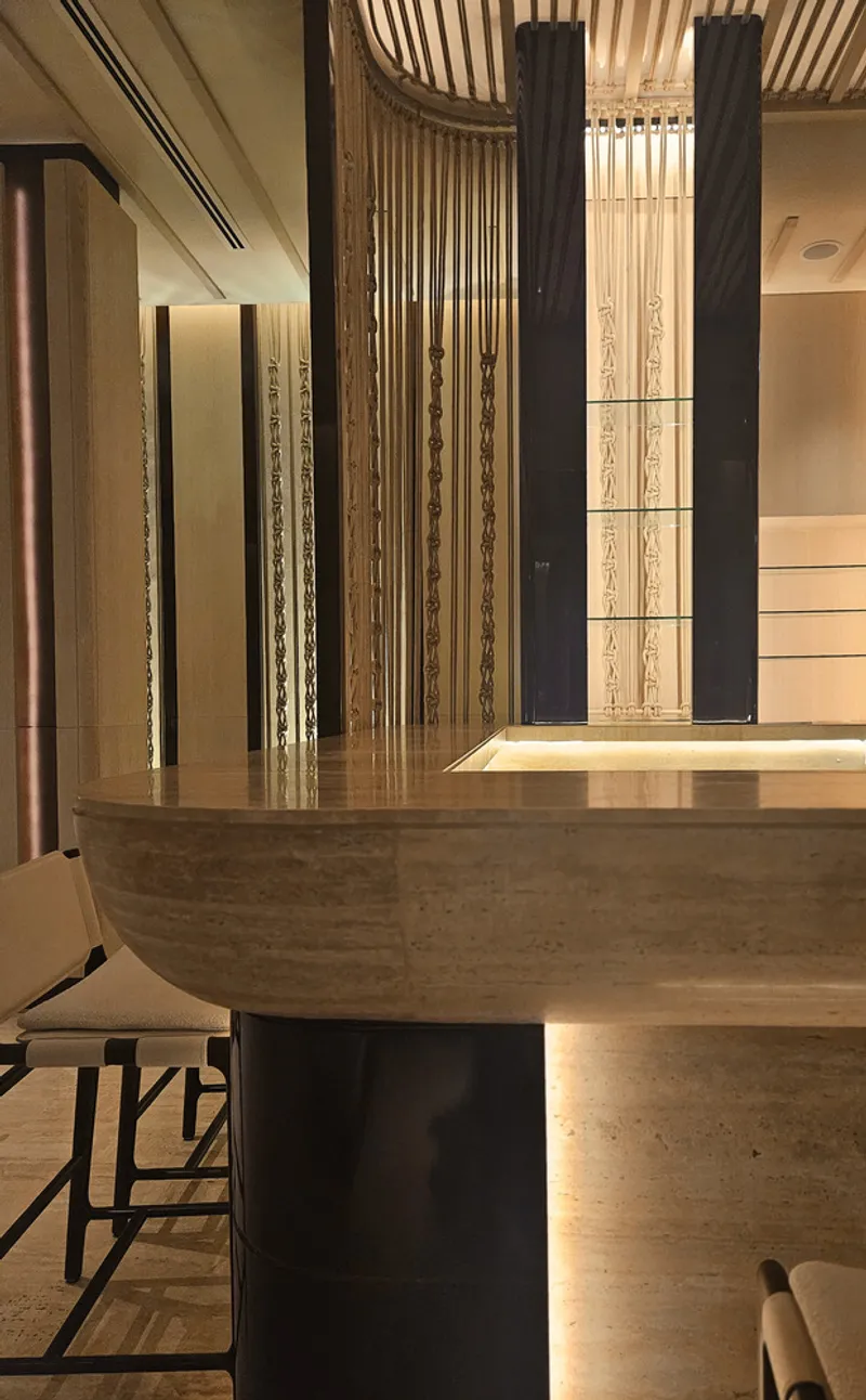 Nalu bar detail at night: sculptural timber counter edge, dark stools, vertical timber screen partition