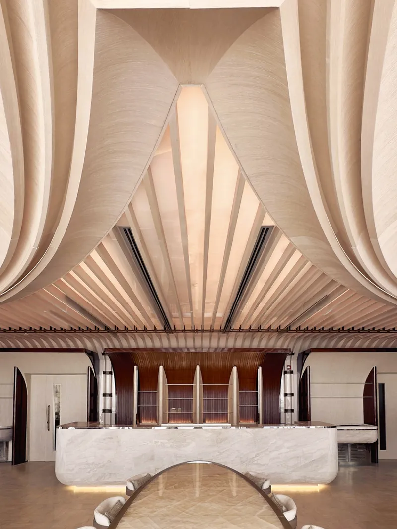 Ilios upper floor: folded ceiling forms converging to a peak above the marble bar, white chairs