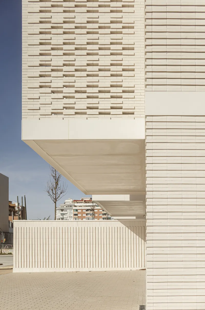 Upper corner: setback terrace at the top floor, vertical metal railing, cream brick facade, blue sky