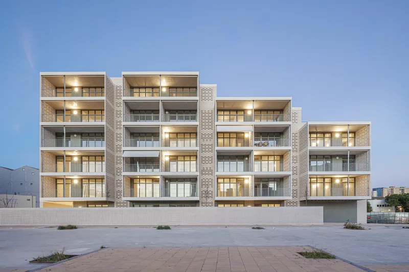 South-west facade at dusk: warm light glowing from the interiors, mountains visible behind, stepped profile, full-width balconies