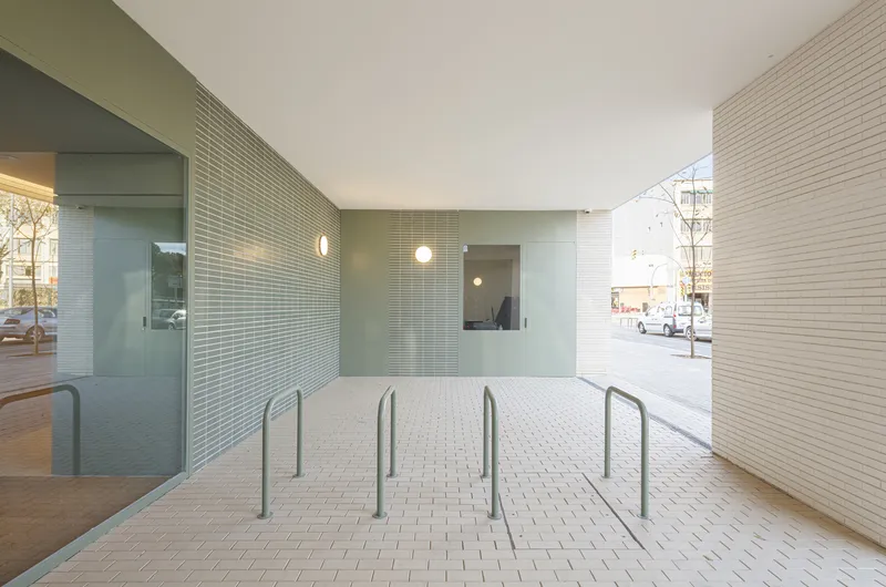 Ground-floor lobby entrance: green glazed tile wall, recessed lighting, bicycle parking rails, paved forecourt, street visible beyond