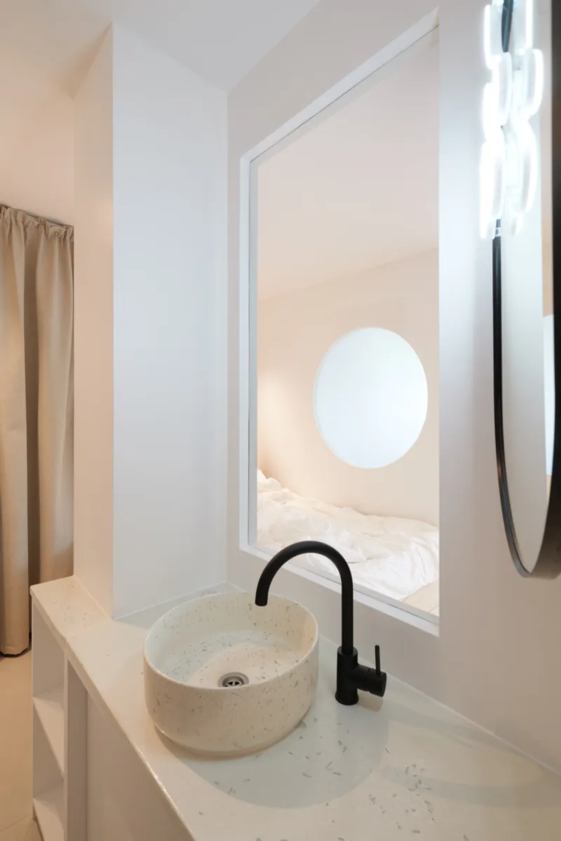 Bathroom detail: close-up of the terrazzo basin and black tap, the round window above looking through to the bedroom alcove