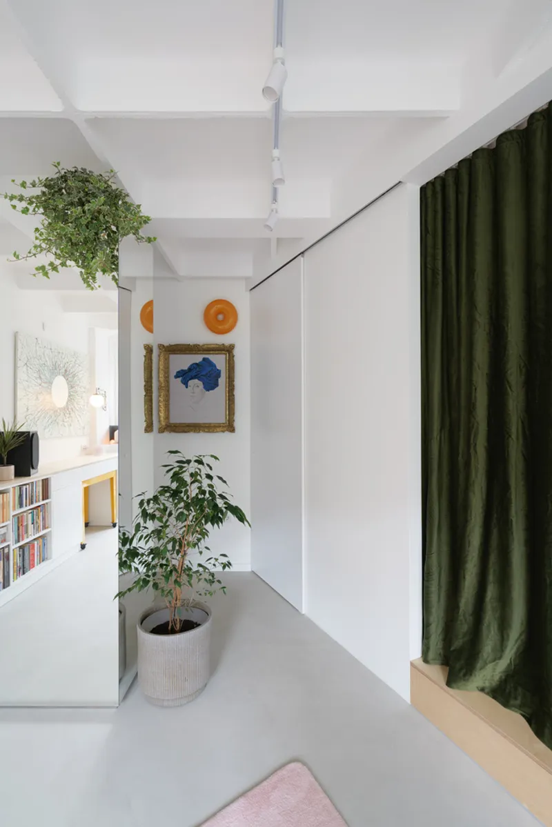 Corridor detail: recessed white door with plants trailing above, green velvet curtain at right, small framed artwork on the wall, minimal white space