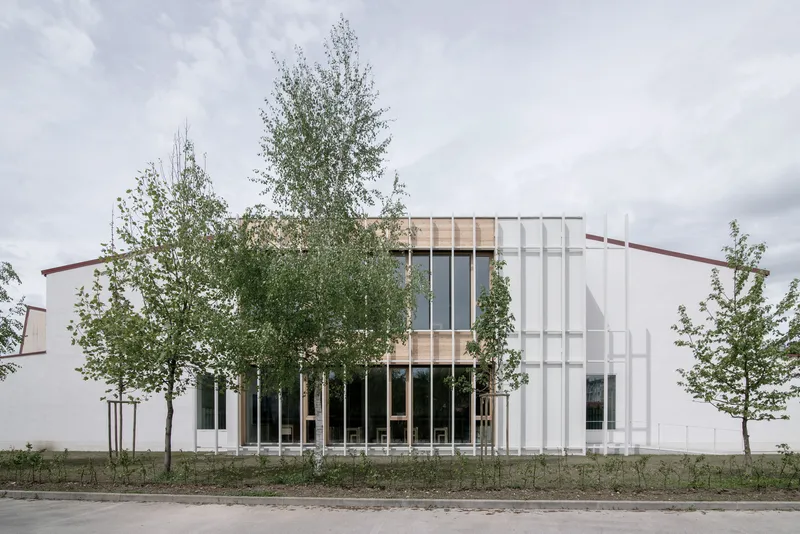 East facade: white vertical metal fins, timber-clad upper storey with full-height glazing, birch trees, overcast sky