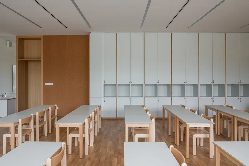 Classroom: rows of timber desks, white lockers along the wall, cork panel, pendant lights, clean and bright