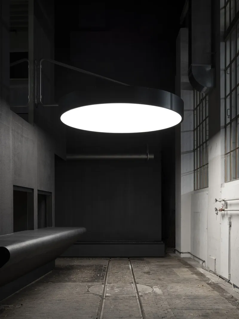 Large circular pendant light suspended above a tiled floor in a double-height lobby