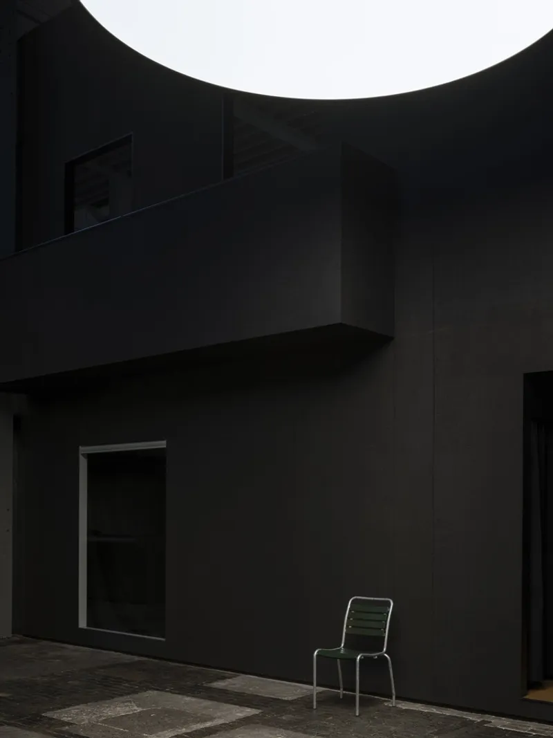 Corner courtyard with overhanging balcony and a single metal chair at dusk