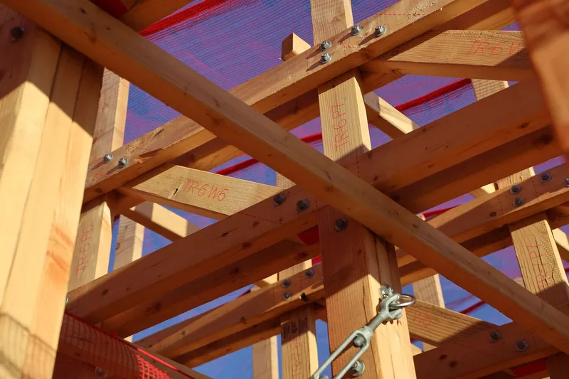 Truss detail: bolted timber joints with robot-inscribed marking numbers (F916), red construction mesh above, steel connectors