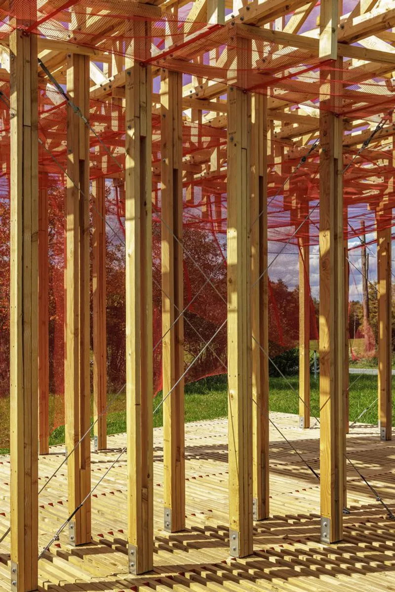 Columns from the deck: vertical timber posts with red mesh curtain hanging between them, dappled afternoon light on the wood slats