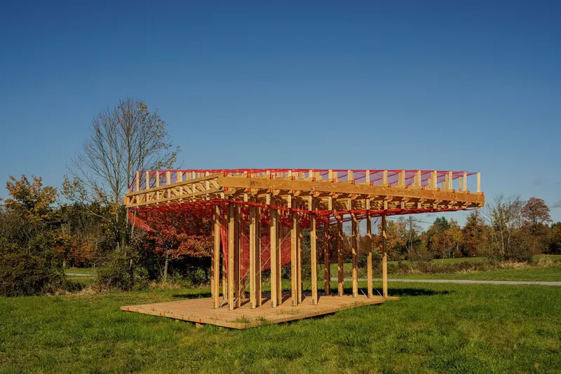 Late-afternoon side view: the pavilion catching warm sunset light, red painted stripes on the timber columns, autumn foliage behind