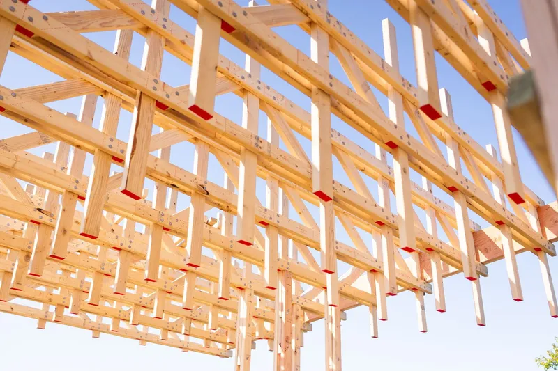 Roof truss detail: repetitive timber trusses with red marking labels left visible as a construction record, extending into perspective