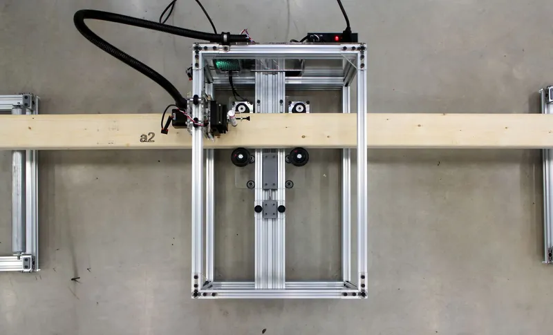 Marking robot: an aluminium gantry frame with a robotic marking head inscribing reference numbers on a timber member in the workshop