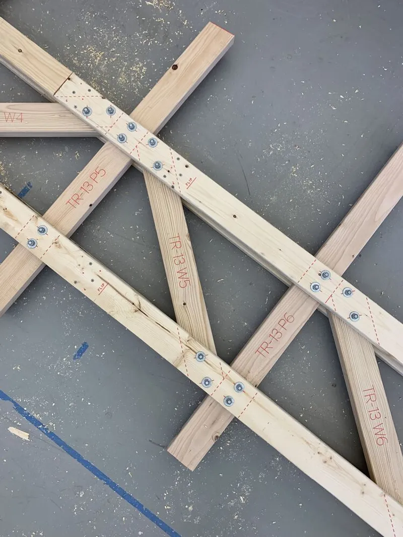 Workshop bench: prefabricated timber truss members laid out with robot-inscribed drilling and connector marks, ready for assembly