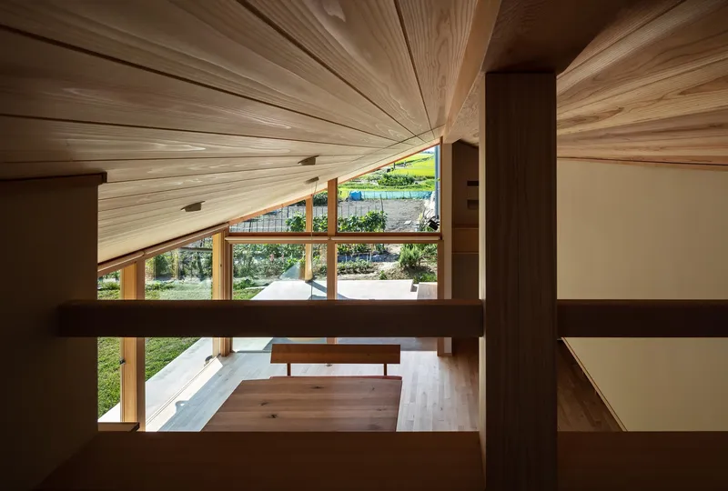Mezzanine view: looking down through cedar columns and railing to the living room, landscape visible through the windows