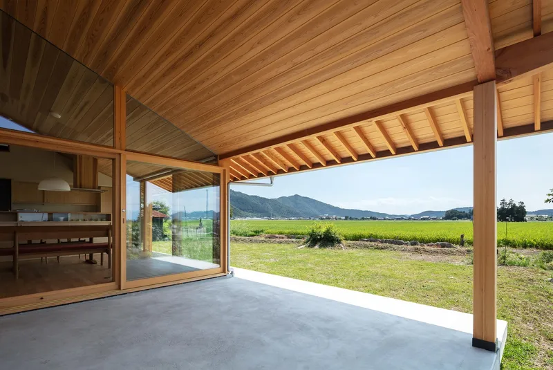Engawa terrace: cedar-lined ceiling extending over concrete deck, full-height glass to interior, rice paddies and mountains beyond