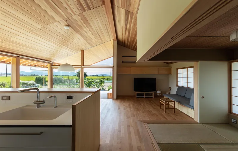 Kitchen and living: cedar ceiling rising to ridge, open-plan kitchen island, sofa, TV unit, tatami room with blue sliding doors beyond
